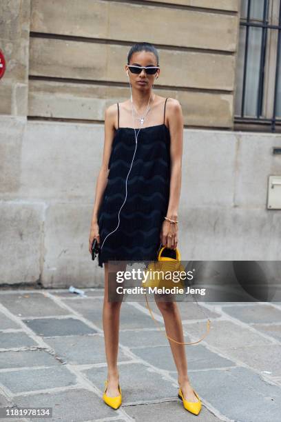 Model Annibelis Baez wears skinny black sunglasses, a black flapper-style fringe bag, yellow purse, and yellow flats after the Dior show during...