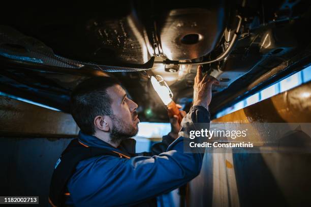 mechaniker, der die unterseite des autos untersucht, während er elektrische lampe hält - elektrische lampe stock-fotos und bilder