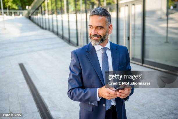 businessman holding the phone in front of a business center - man side way looking stock pictures, royalty-free photos & images