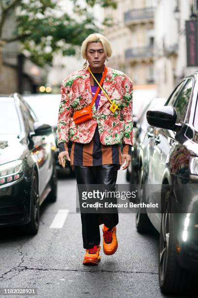 Yu Masui wears earrings, a green and pink tigers print oversized jacket, a brown top with large black stripes, a tiny yellow crossbody bag, an orange...