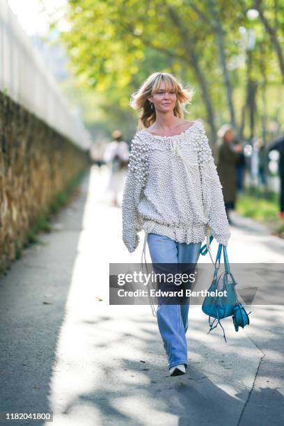 Jeanette Madsen wears a white bejewelled top with attached pearls, a blue Loewe bag, white pointy shoes, blue flared denim pants, outside Loewe,...