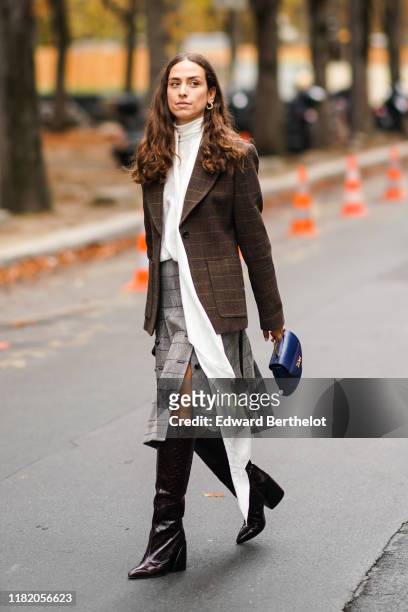 Erika Boldrin wears earrings, a checked brown blazer jacket, a white top with a long scarf, a gray skirt, leather boots, a blue bag, outside Chloe,...