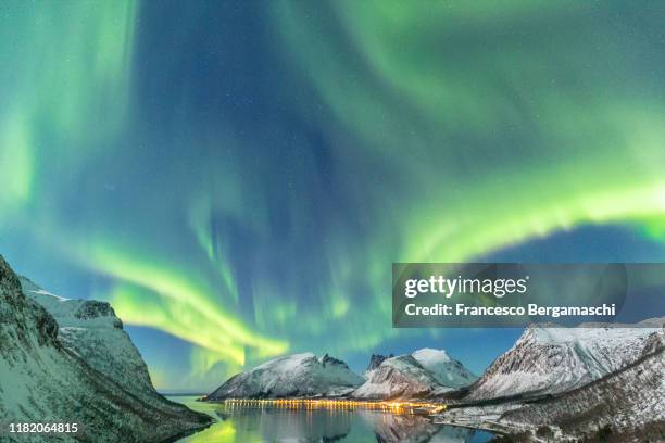 the aurora borealis lights up in the sky and is reflected in the fjord. northern norway, europe. - aurora borealis lofoten stock-fotos und bilder