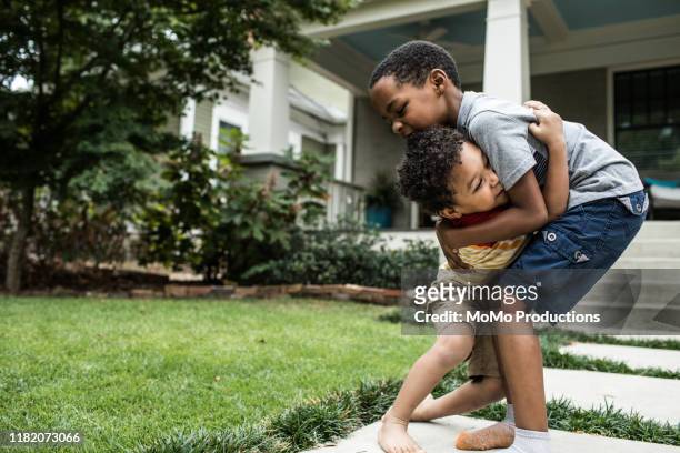 two boys (3 yrs and 6 yrs) playing in front of house - boys wrestling stock pictures, royalty-free photos & images
