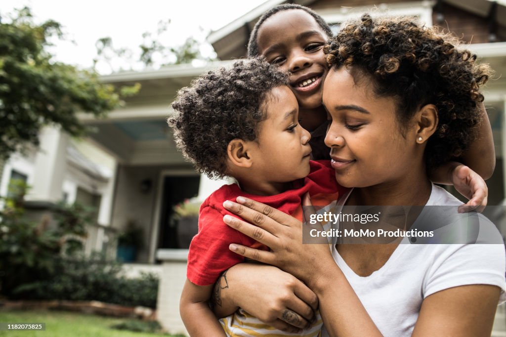 Single mother playing with young sons in front of house