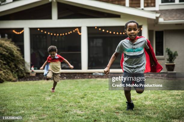 young boys (3 yrs and 6yrs) in capes playing in backyard - running kinderen stockfoto's en -beelden