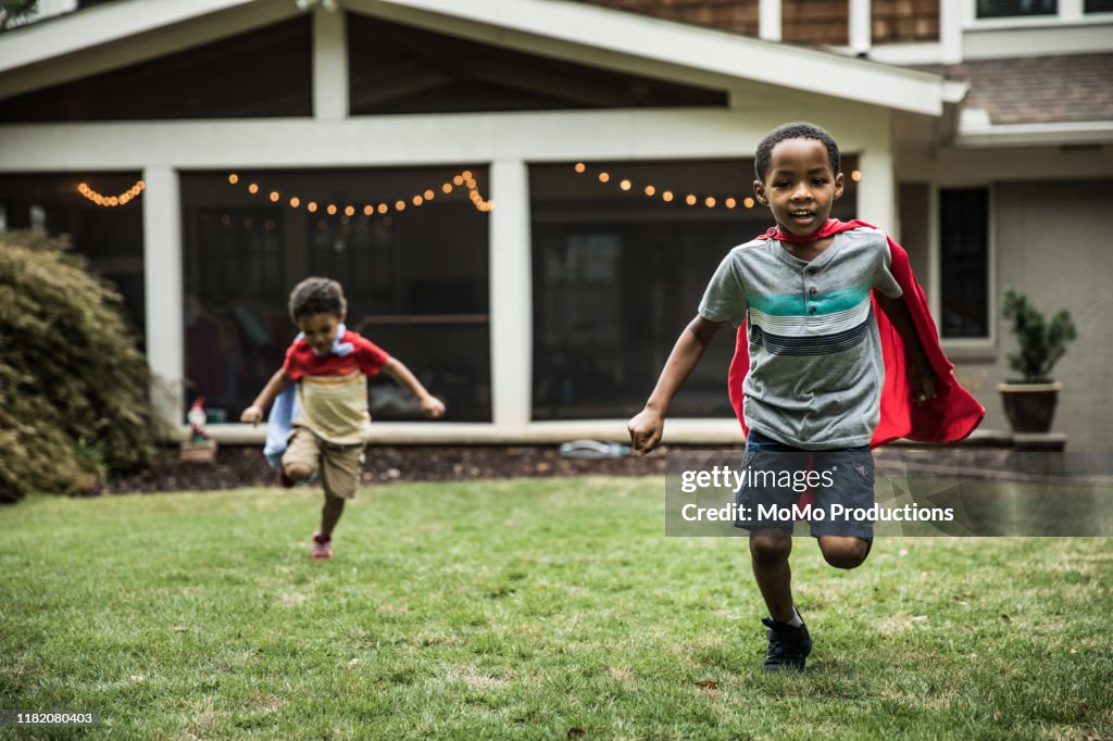 Young boys (3 yrs and 6yrs) in capes playing in backyard