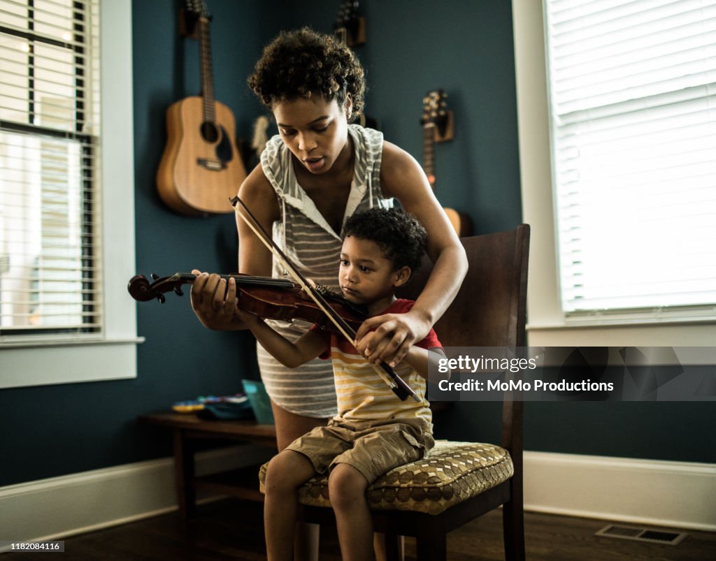 Mother helping young boy (3 yrs) practice violin