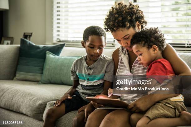 Single mother using tablet with young sons on couch