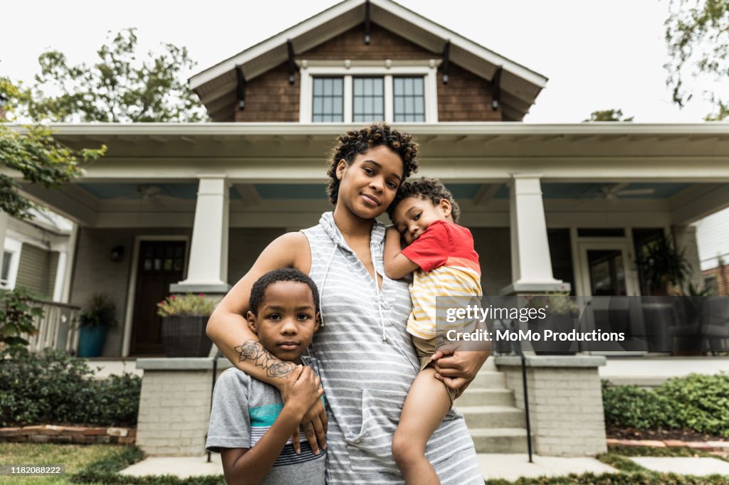 Portrait of single mother with young sons in front of house