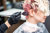 Hairdresser hand in black gloves paints the woman's hair in a pink color.