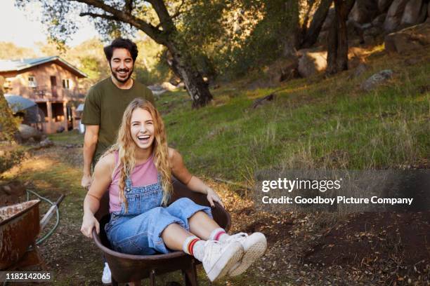 laughing woman being pushed by her boyfriend in a wheelbarrow - wheelbarrow stock pictures, royalty-free photos & images