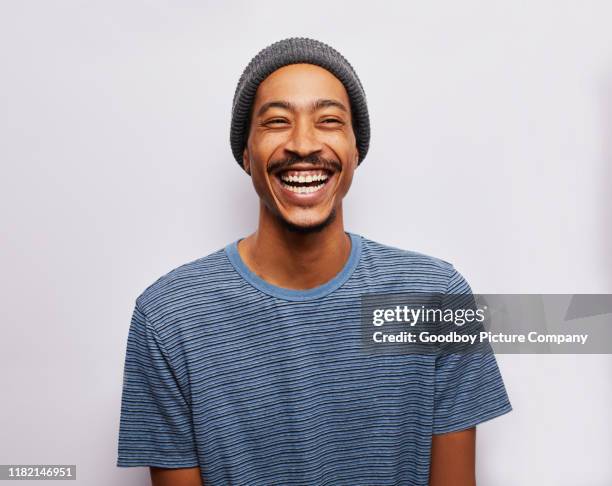 laughing young man standing against a gray background - black hat stock pictures, royalty-free photos & images