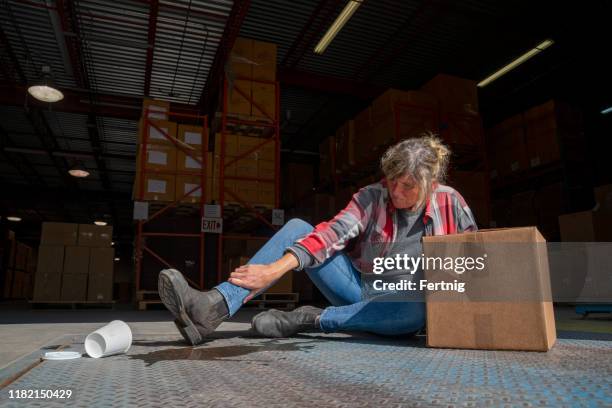een magazijn, logistiek veiligheids onderwerp. een vrouwelijke werknemer valt na het uitglijden op een gemorst drankje. - val stockfoto's en -beelden