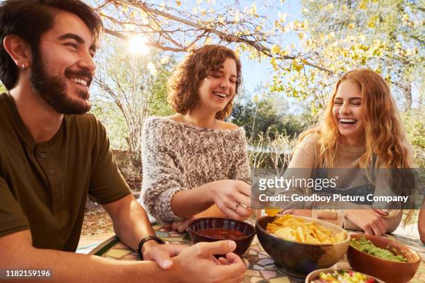 lachende freunde essen an einem sonnigen nachmittag gemeinsam draußen - snacks stock-fotos und bilder
