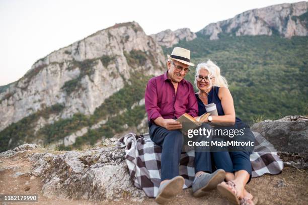 loving senior couple hiking, sitting on the top of rock, exploring. active mature man and woman hugging and happily smiling. - woman sitting top man stock pictures, royalty-free photos & images