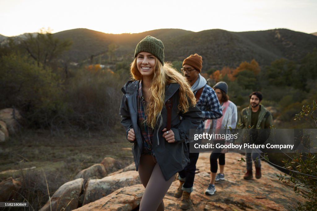 Smiling young woman and friends hiking up a hill together