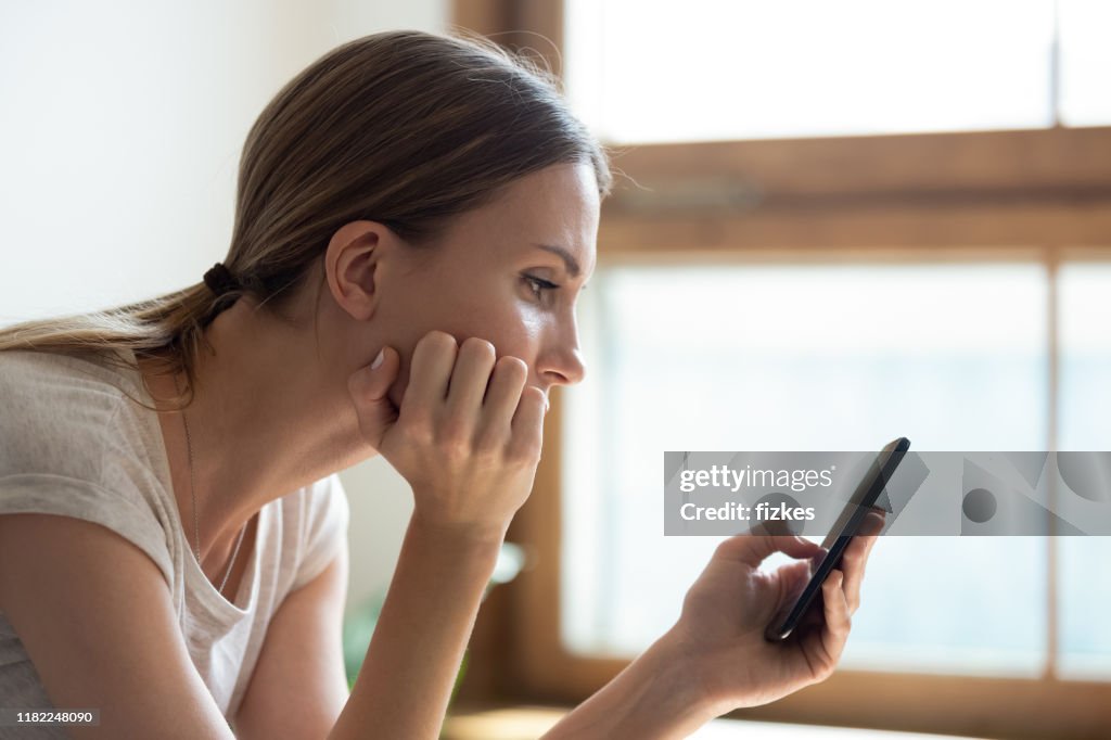 Pensive sad young woman holding smartphone waiting sms from boyfriend