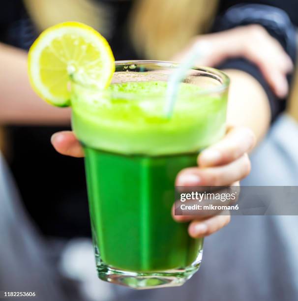 hand of woman holding a glass of green smoothie - kweekgras stockfoto's en -beelden