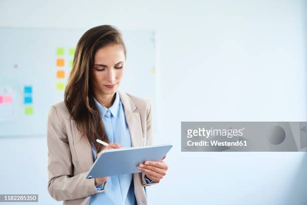 young businesswoman writing on tablet in office - digitized pen stock-fotos und bilder