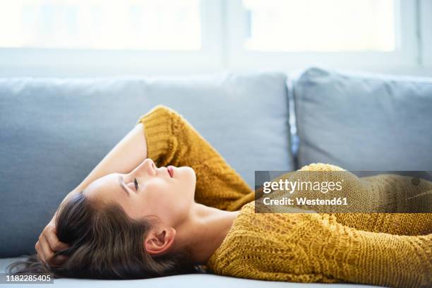 young woman lying on sofa with eyes closed and relaxing - women lying imagens e fotografias de stock