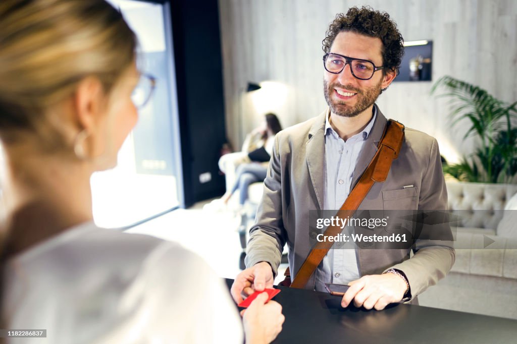 Smiling businessman handing over credit card at reception
