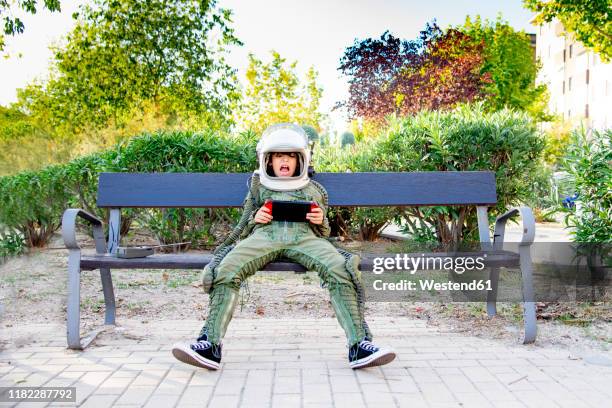 boy wearing a space suit and sitting on a bench, using tablet - super excited suit stock pictures, royalty-free photos & images