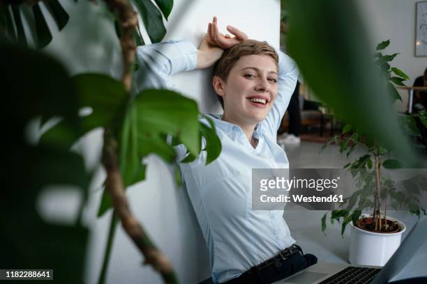 portrait of a businesswoman with laptop sitting on the floor surrounded by plants - omgeven stockfoto's en -beelden