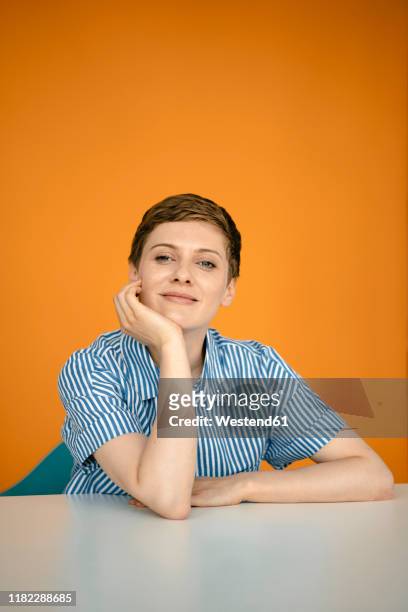 portrait of woman leaning on table with orange background - kin in de hand stockfoto's en -beelden