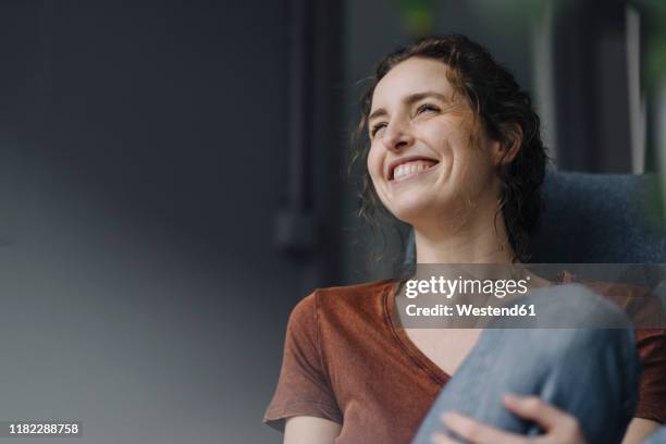 portrait of laughing young woman sitting on lounge chair at home - at home portrait fotografías e imágenes de stock