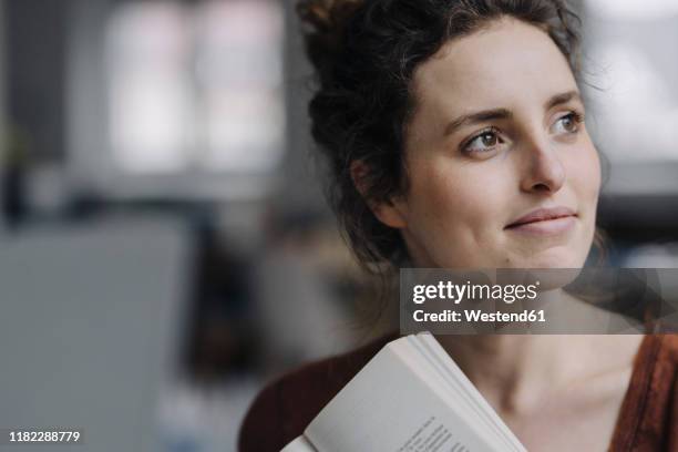 portrait of smiling young woman with book looking at distance - fossetta foto e immagini stock