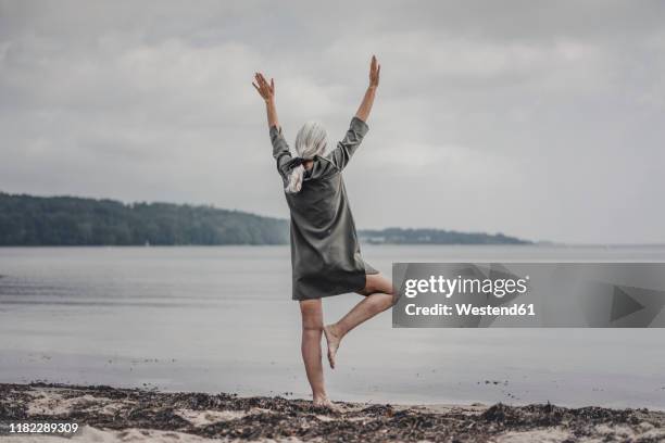 senior woman looking at sea, standing on one leg, rear view - on one leg stock pictures, royalty-free photos & images