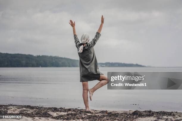 senior woman looking at sea, standing on one leg, rear view - stå på ett ben bildbanksfoton och bilder