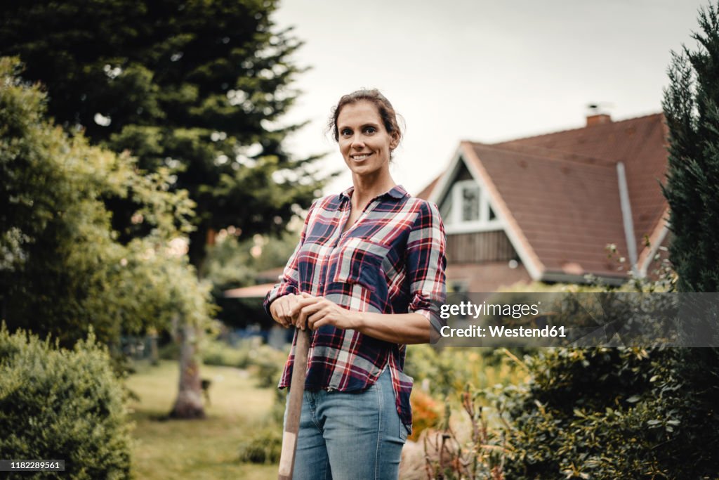 Proud home owner standing in her garden with a spade