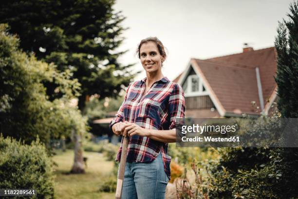 proud home owner standing in her garden with a spade - mid adult women stock pictures, royalty-free photos & images