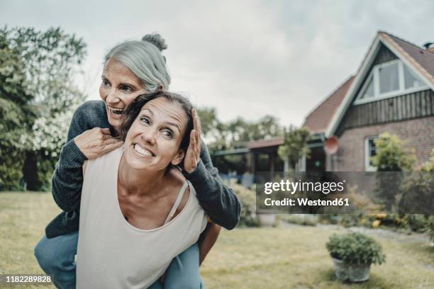 daughter carrying mother piggaback in the garden - menschliches alter stock-fotos und bilder