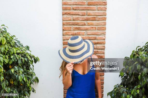 woman wearing blue dress and straw hat standing in front of wall, nerja, spain - escote fotografías e imágenes de stock