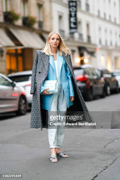 Leonie Hanne wears a long coat with printed geometrical patterns and shoulder pads, a blue blazer jacket, a quilted pale blue bag, a white top, pale...