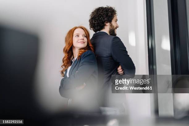 confident businessman and businesswoman standing back to back in office - rücken an rücken stock-fotos und bilder