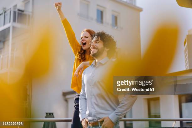 woman with colleague on roof terrace clenching fist - business couple stockfoto's en -beelden
