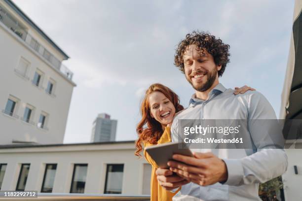 two happy colleagues with tablet on roof terrace - paar draussen nicht winter stock-fotos und bilder