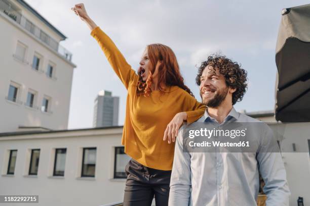 woman with colleague on roof terrace clenching fist - uomo donna per mano foto e immagini stock