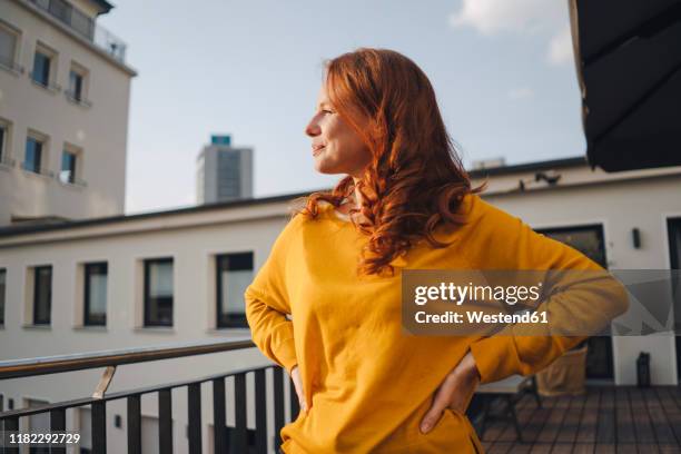 redheaded woman standing on roof terrace - frau balkon stock-fotos und bilder