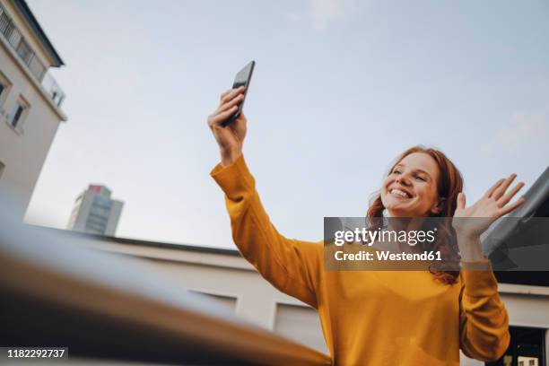 smiling redheaded woman using cell phone on roof terrace - relation à distance photos et images de collection