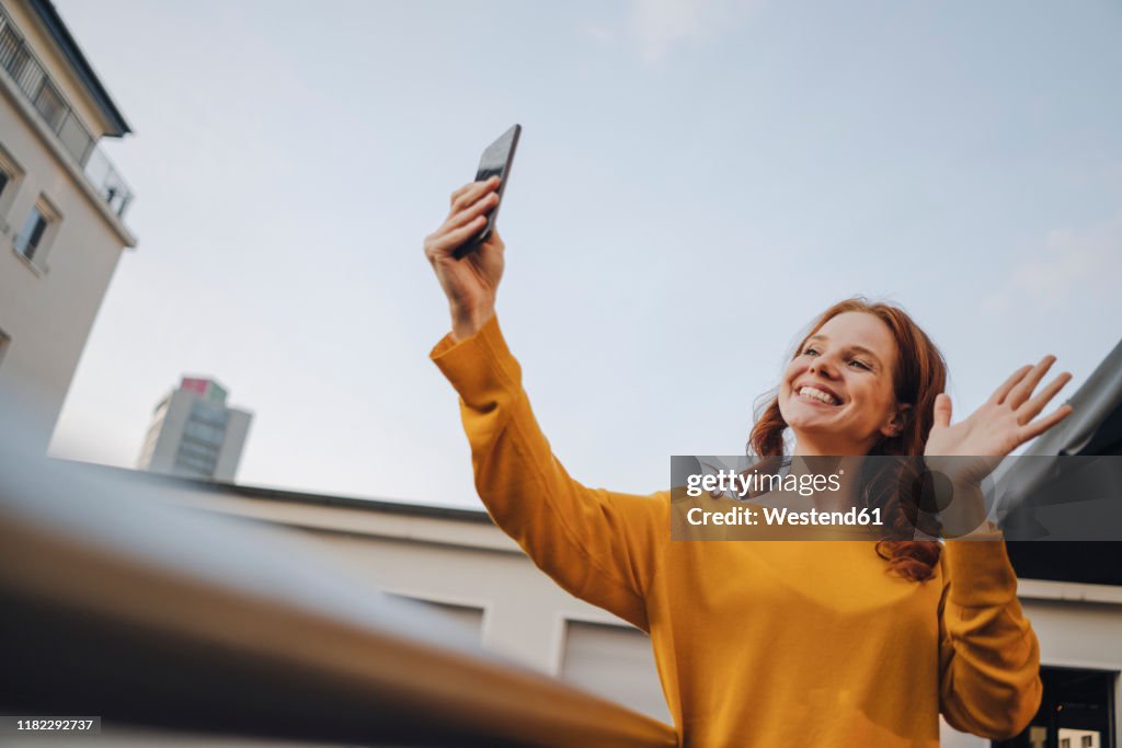 Smiling redheaded woman using cell phone on roof terrace