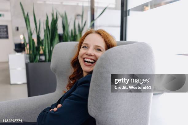 happy redheaded businesswoman sitting in armchair - lounge chair stock-fotos und bilder