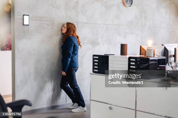 tired businesswoman leaning against a wall in office - fatigue full body stock pictures, royalty-free photos & images