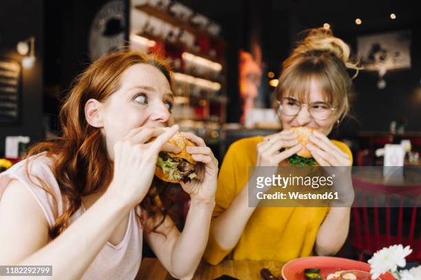 two female friends eating burger in a restaurant - adults eating hamburgers foto e immagini stock