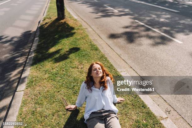 redheaded woman sitting on grass verge - grass shoulder stock pictures, royalty-free photos & images