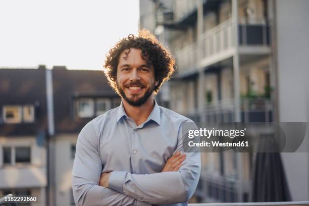 portrait of smiling businessman on roof terrace - gekruld haar stockfoto's en -beelden